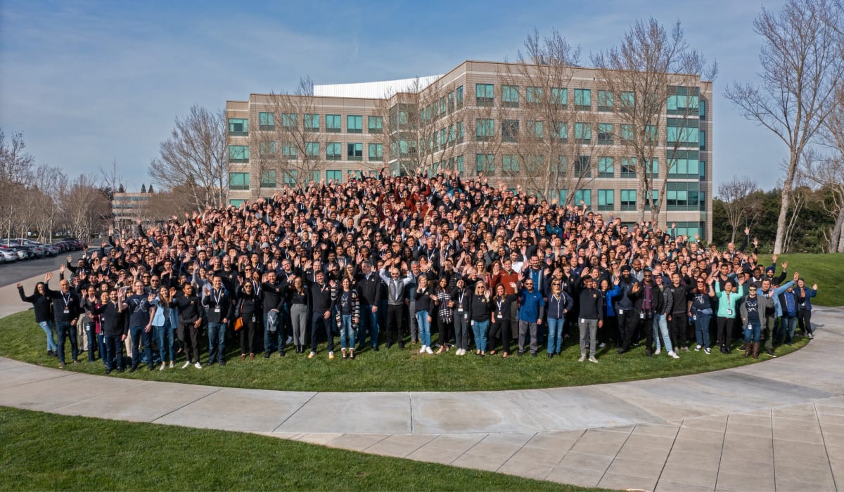 A huge group of 10x employees are standing together in front of the headquarters in Pleasanton, CA, waving at the camera